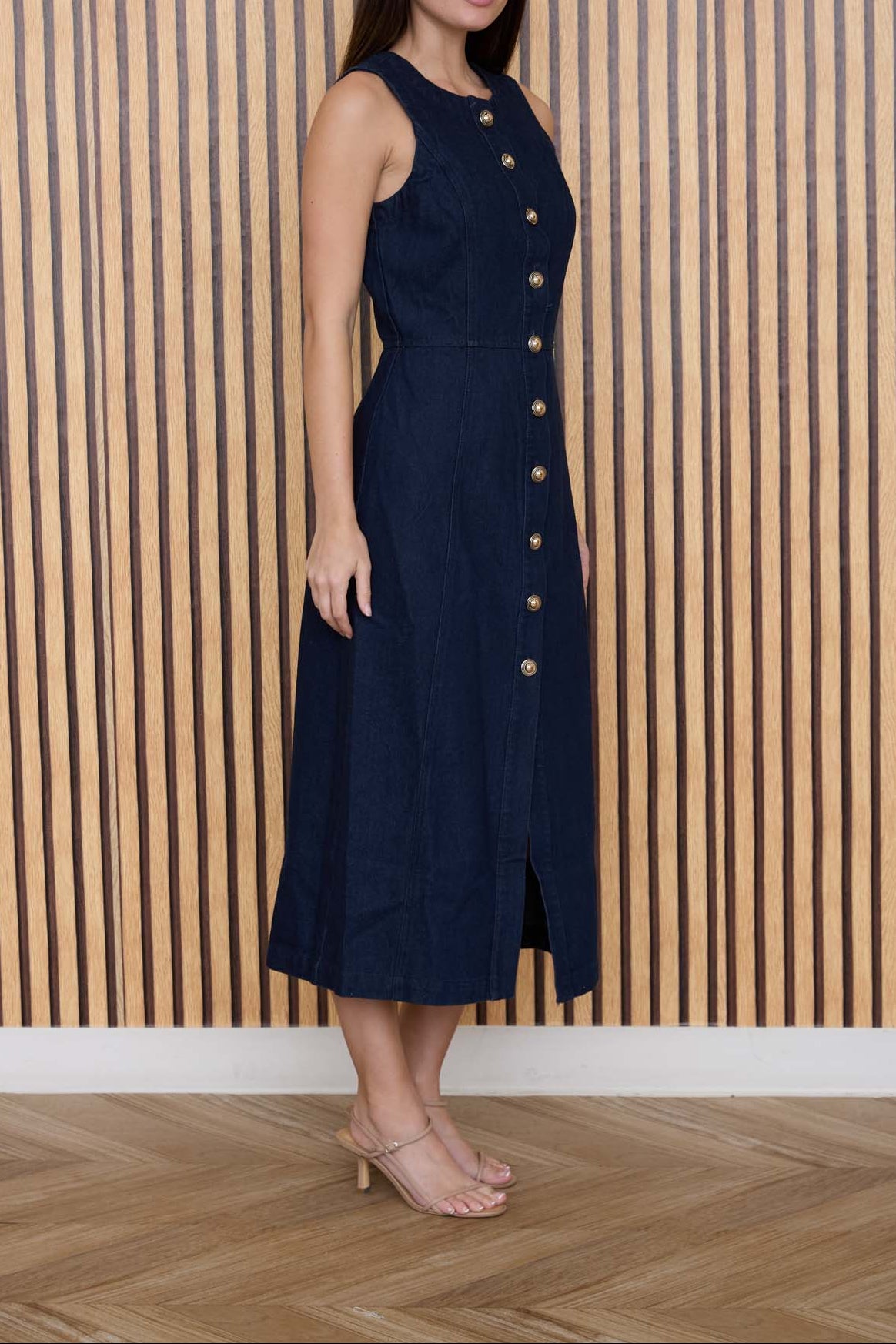 Woman wearing a navy dress with buttons against a wooden paneled wall.