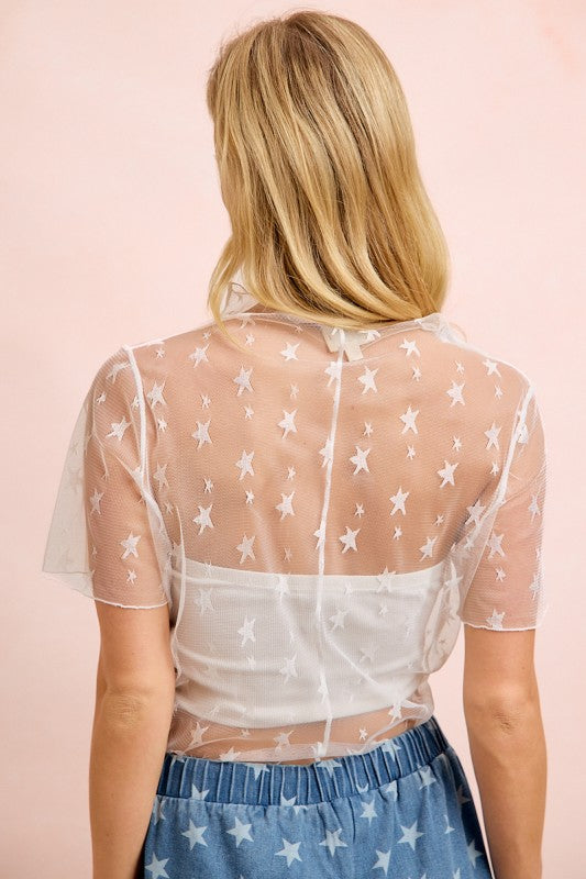 Woman wearing a sheer white top with star patterns on a pink background
