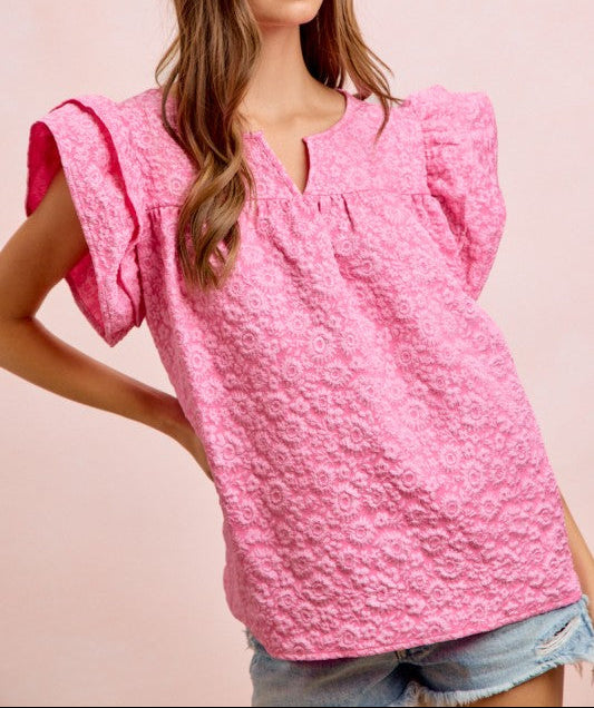 Woman wearing a pink textured blouse with ruffled sleeves on a light pink background
