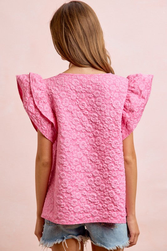 Pink textured top with ruffled sleeves worn by a person on a pink background