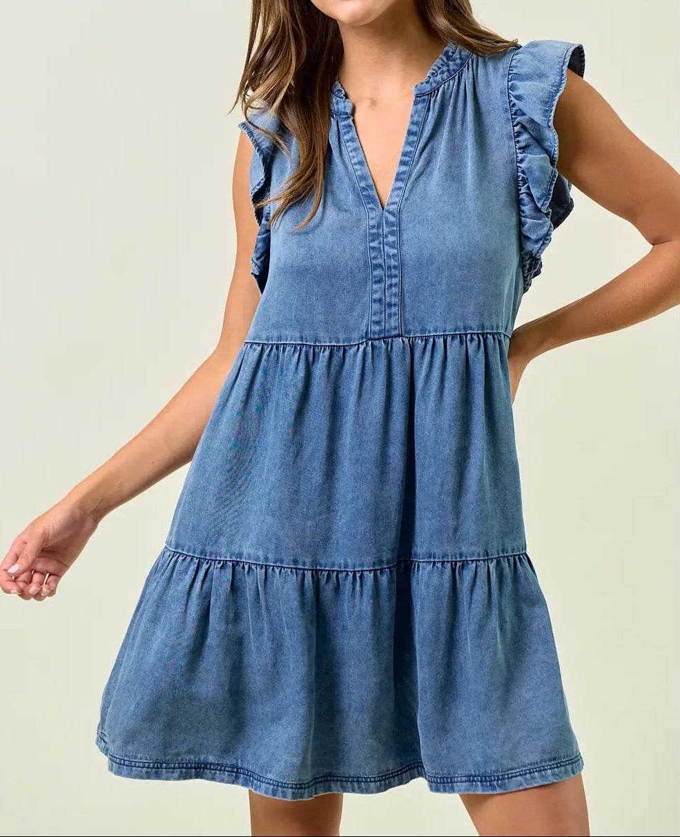 Woman wearing a denim dress with ruffled sleeves on a plain background