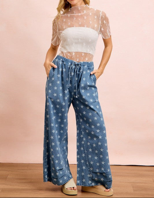 Woman wearing a sheer top and blue star-patterned pants on a pink background