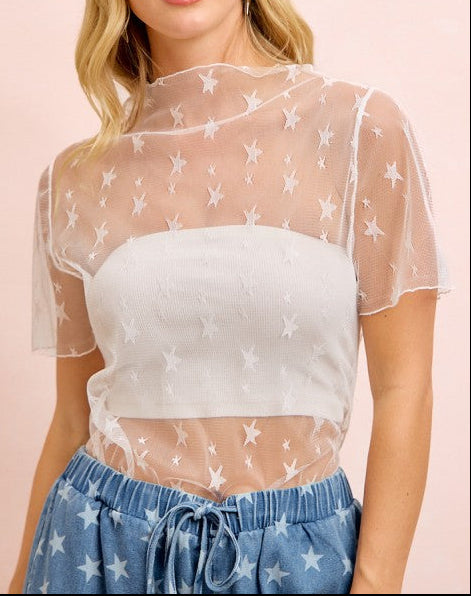 Woman wearing a sheer top with star patterns and blue pants on a pink background