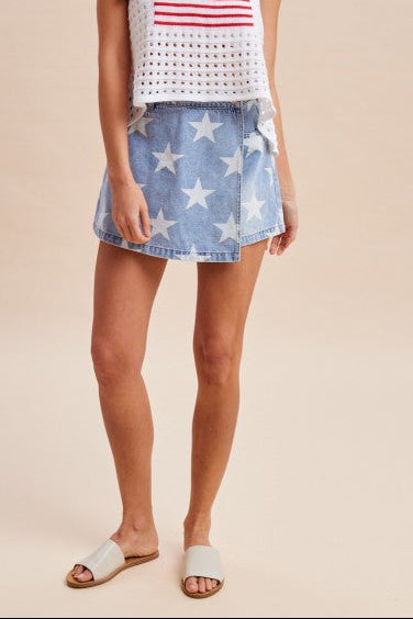 Woman wearing a white tank top with an American flag design and a denim skirt with star pattern on a beige background