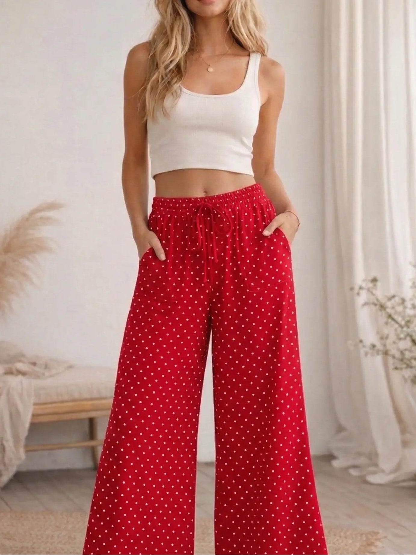 Woman wearing a white crop top and red polka dot pants in a bright room.