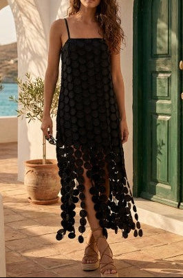 Woman in a black dress with pom-pom details standing on a sunlit patio with ocean view.