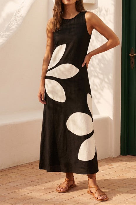 Woman wearing a black dress with white patterns standing against a white wall.