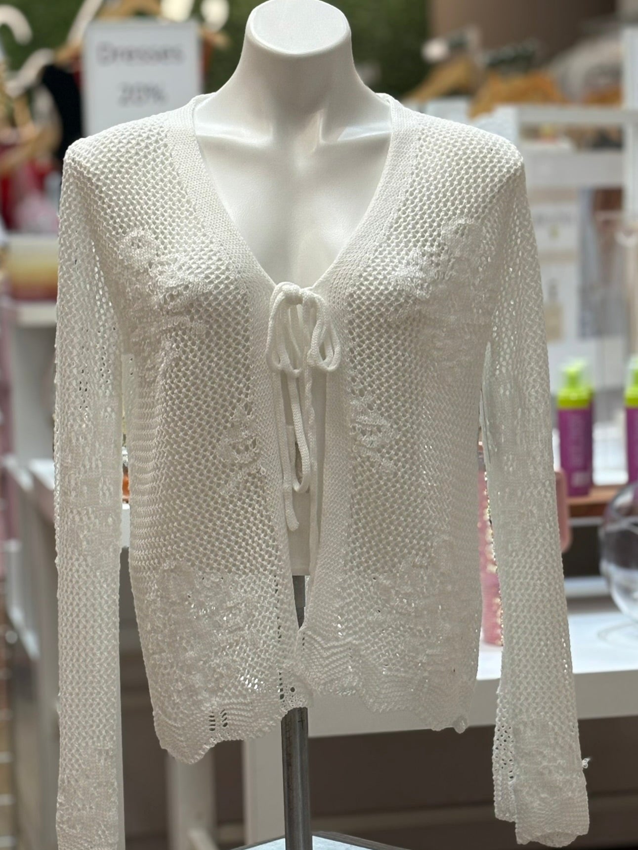 White open-knit or crochet material cardigan on a mannequin in a store setting