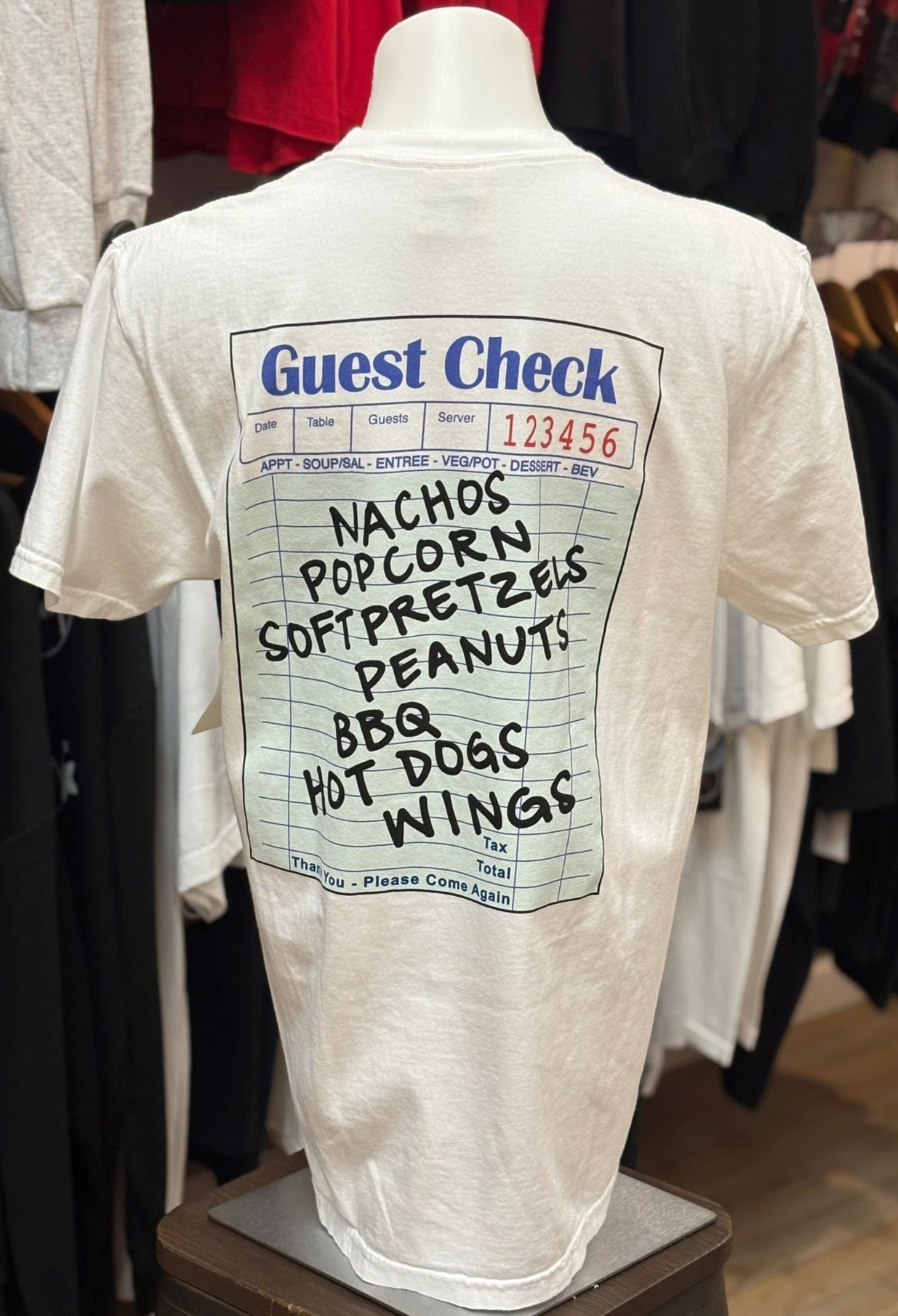 White t-shirt with a humorous 'Guest Check' design on a mannequin in a store setting.