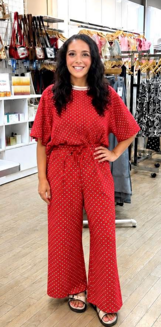 Woman in a red patterned jumpsuit standing in a store with clothing racks in the background.