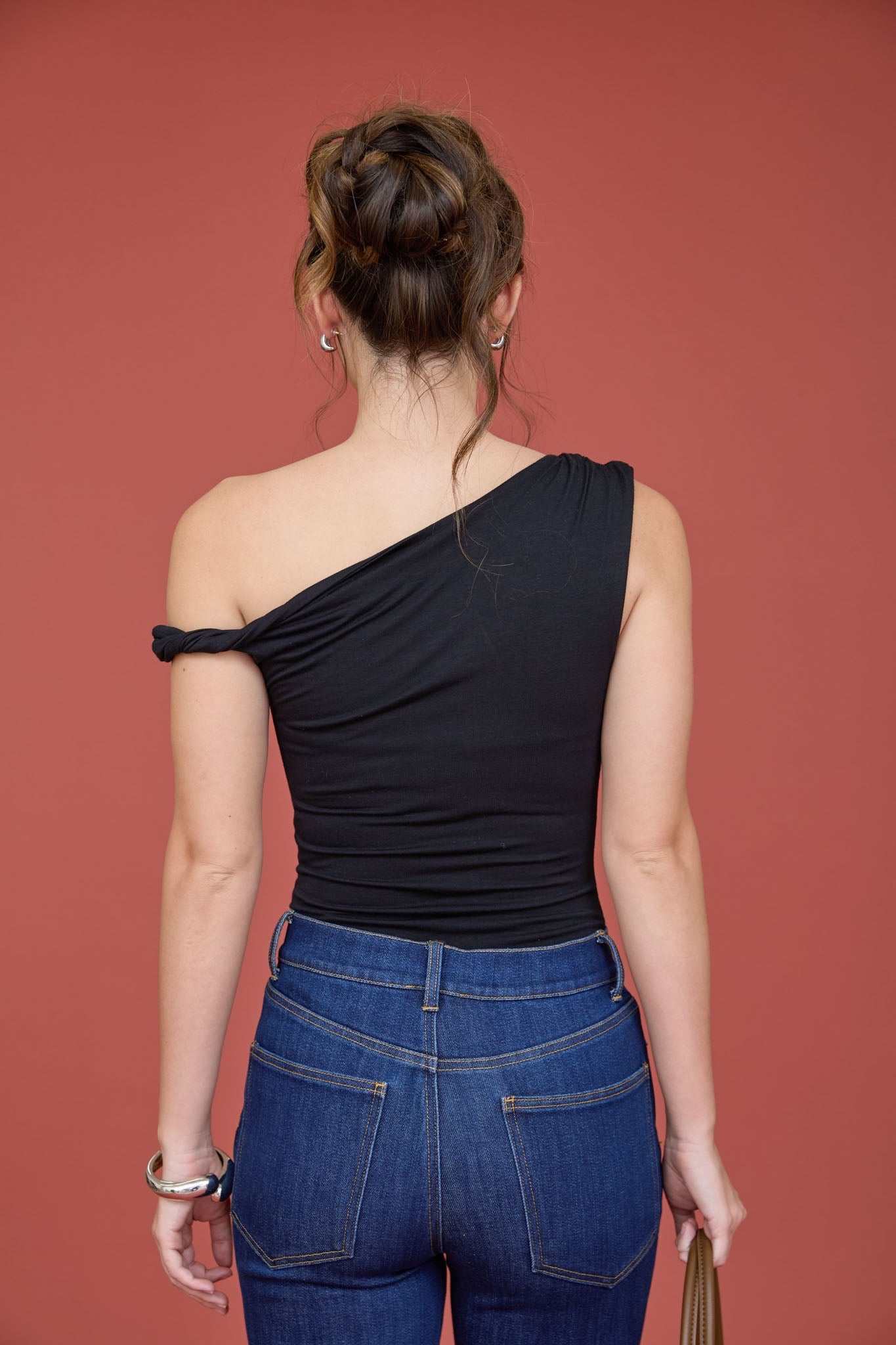 Woman wearing a black one-shoulder top and blue jeans against a red background