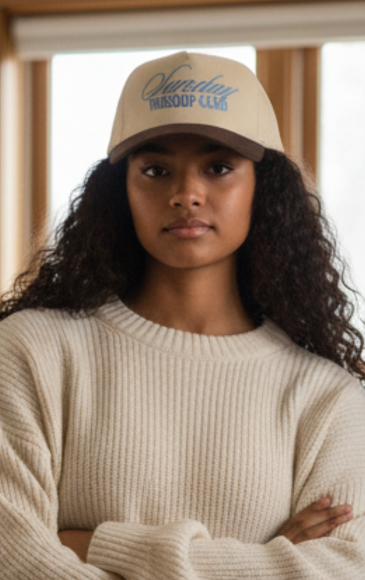Woman wearing a beige cap and sweater in a room with wooden beams.