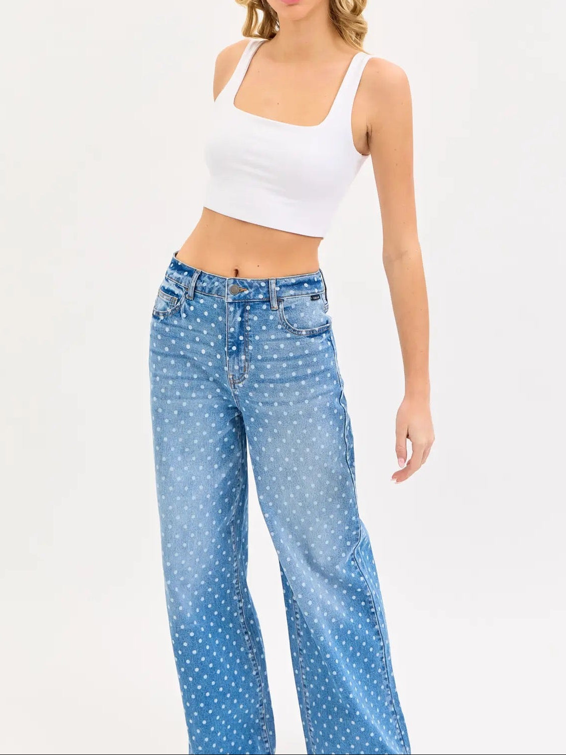 Woman wearing a white tank top and blue polka dot jeans on a white background