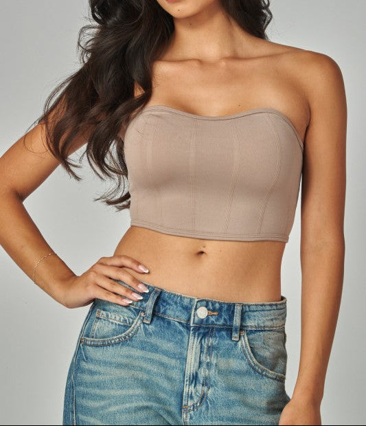 Woman wearing a beige strapless top and blue jeans against a gray background