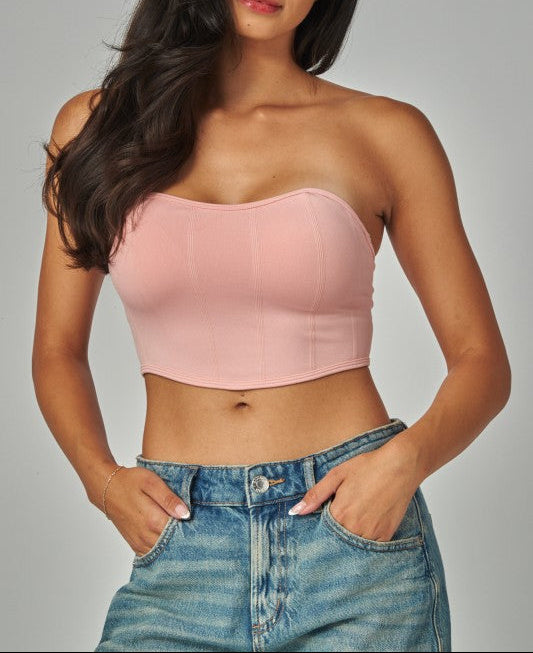 Woman wearing a pink strapless top and blue jeans against a gray background