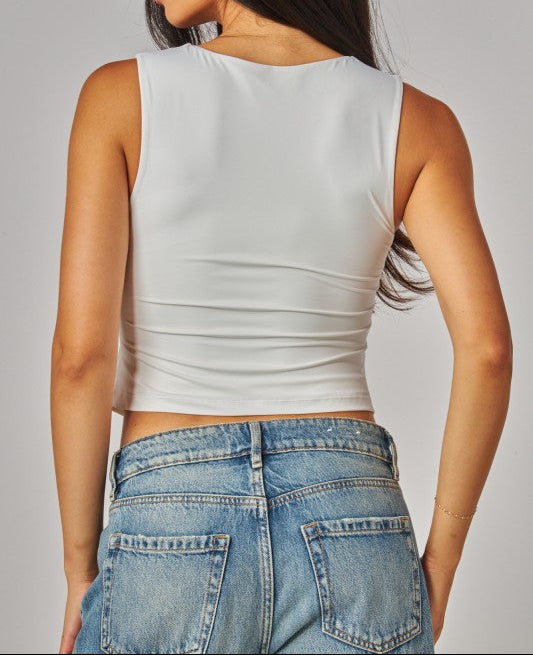 Woman wearing a white sleeveless top and blue jeans on a plain background