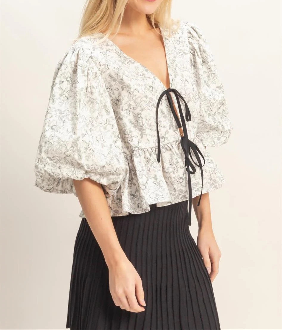 Woman wearing a floral blouse with puff sleeves and a black pleated skirt on a plain background
