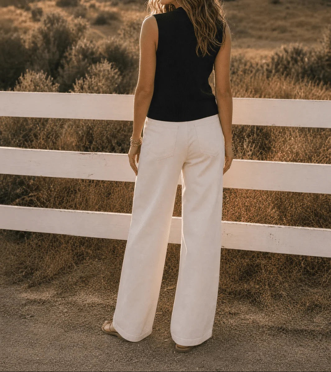 Woman standing by a white fence in a desert landscape at sunset