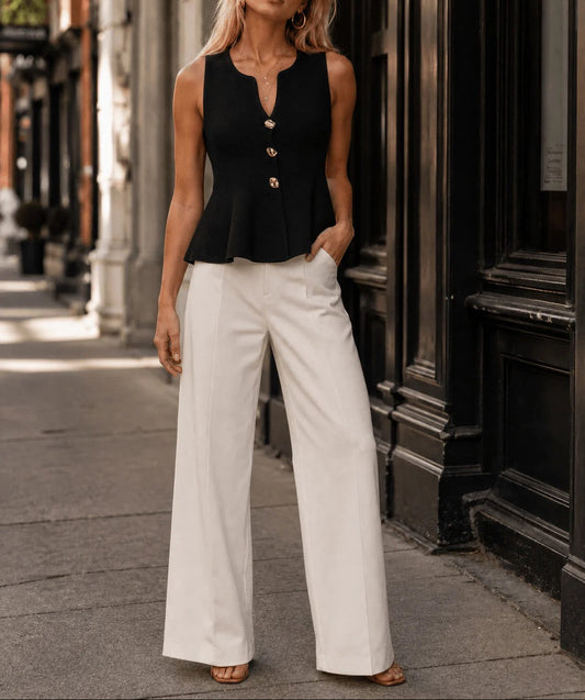 Woman wearing a black sleeveless top with buttons and white pants on a city street.