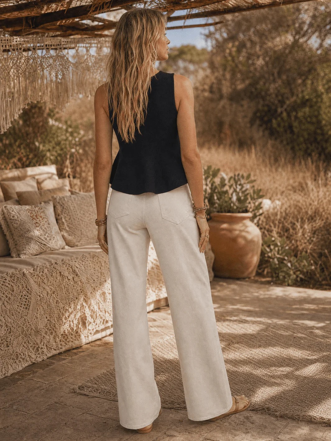 Woman standing in a sunlit outdoor setting with a couch and plants.