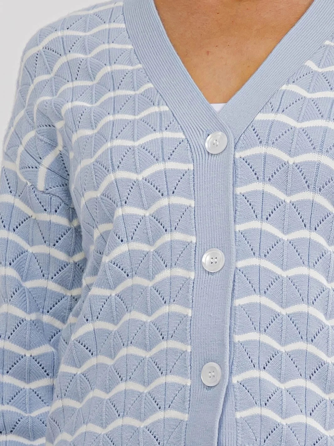 A close-up of a light blue and white patterned knit cardigan with a V-neck and three white buttons.