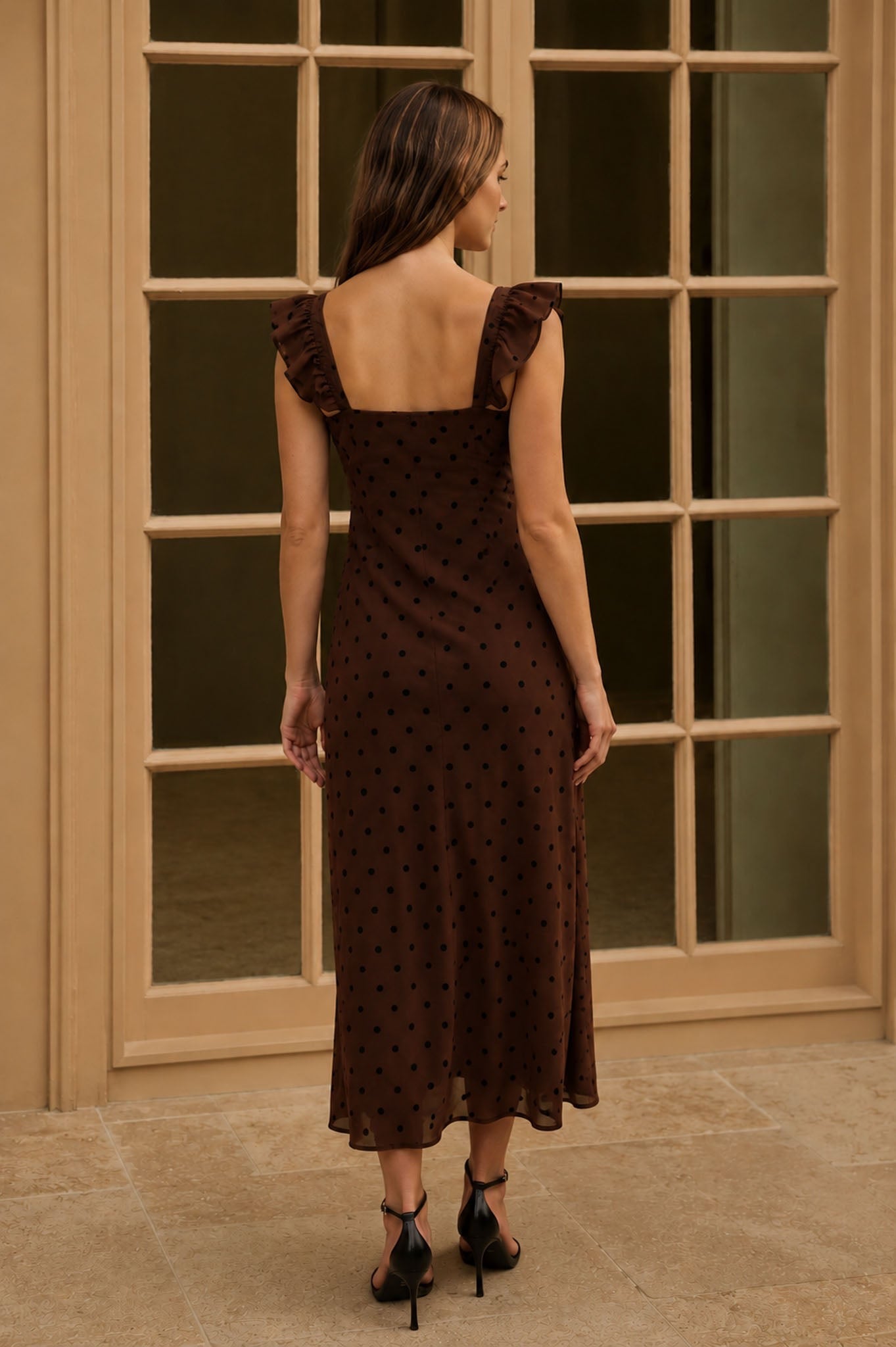 Woman wearing a brown polka dot dress standing in front of a glass door.