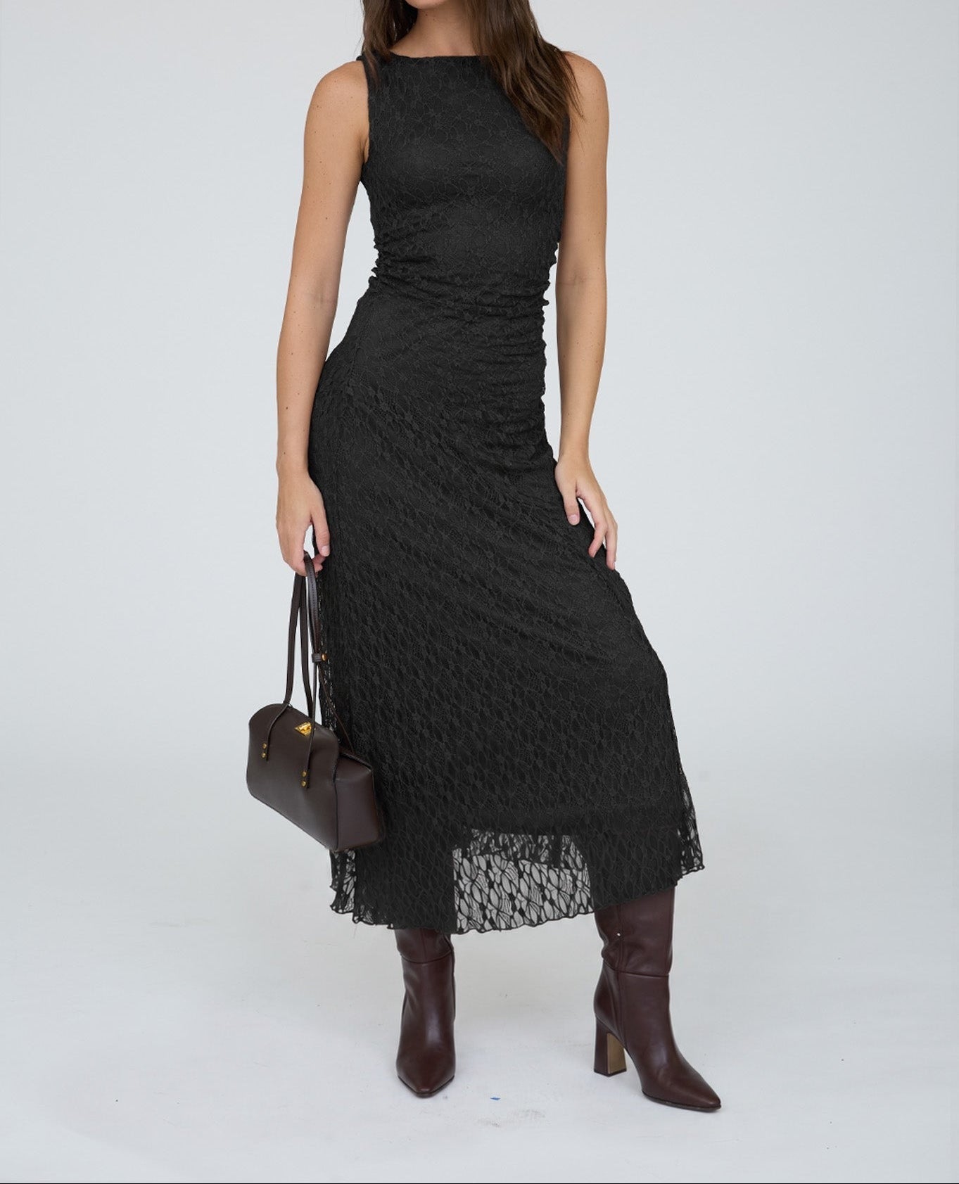 A woman modeling a sleeveless black midi dress with a textured, ribbed knit pattern and a sheer lace hem, styled with dark brown leather knee-high boots and a dark brown handbag against a light gray studio background.