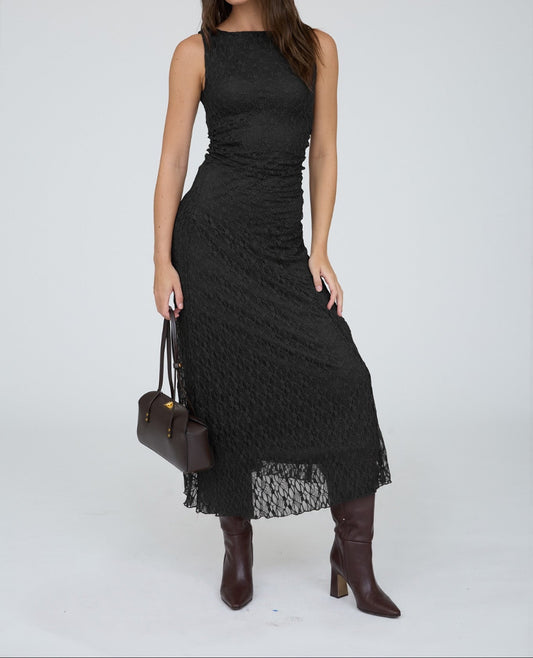 A woman modeling a sleeveless black midi dress with a textured, ribbed knit pattern and a sheer lace hem, styled with dark brown leather knee-high boots and a dark brown handbag against a light gray studio background.