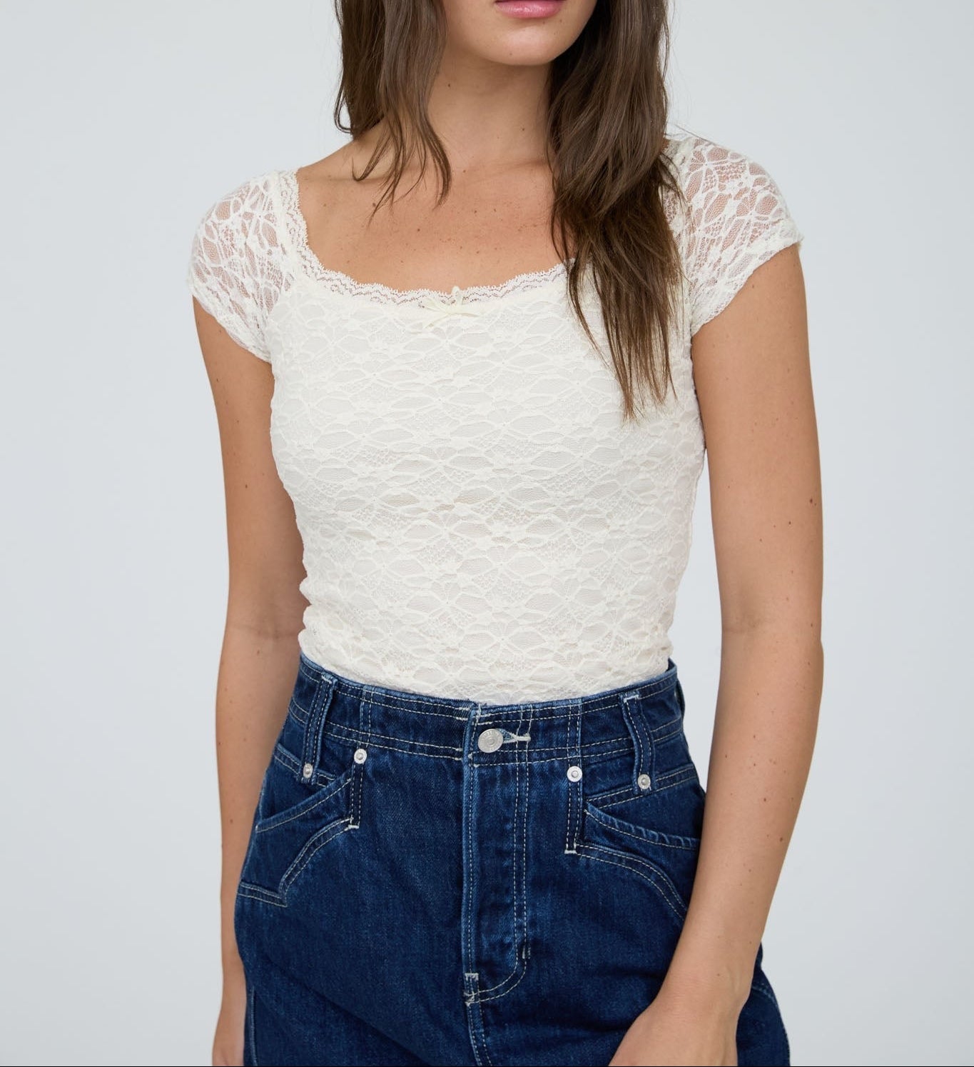 Woman wearing a white lace top and blue jeans against a plain background