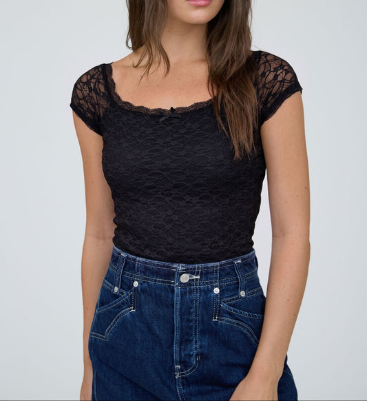 Woman wearing a black lace top and blue jeans against a plain background
