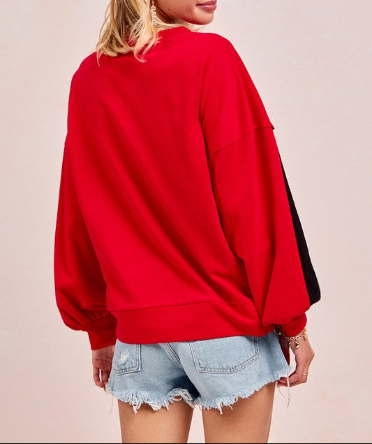 A woman shown from the back wearing a bright red oversized sweatshirt with black side panels, paired with light blue denim shorts, against a solid pale pink background.