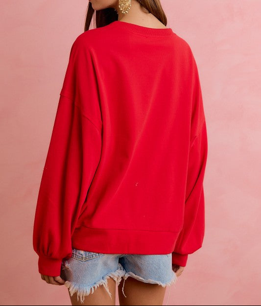 A woman wearing a bright red crewneck sweatshirt and light blue denim shorts, shown from a back-three-quarter view against a solid pink background.