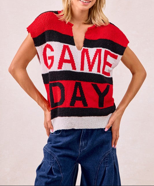 A woman modeling a short-sleeve knit sweater with bold horizontal red, black, and white stripes and the words 'GAME DAY' across the front, paired with blue jeans against a plain light background.
