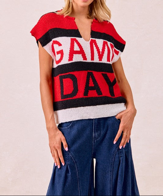 A woman wearing a red, black, and white striped knit sweater with 'GAME DAY' written across the front, paired with blue wide-leg jeans, against a light beige background.