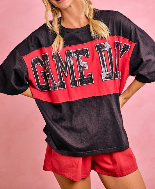 Woman wearing a black and red 'GAME ON' oversized shirt with red shorts on a pink background