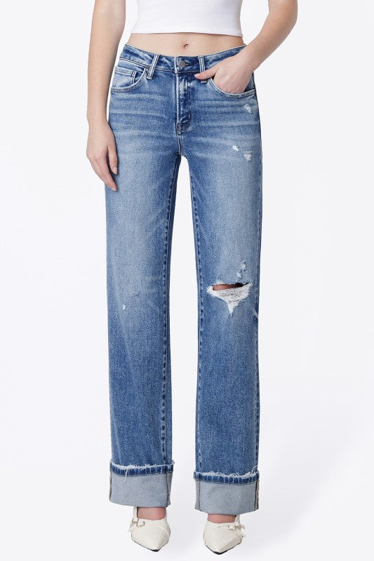 A model wearing a pair of light blue, straight-leg denim jeans with distressed details and rolled cuffs, paired with a white crop top and white pointed-toe heels.
