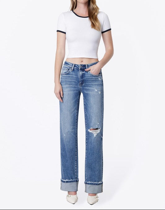 A woman modeling a white short-sleeve crop top with black trim and light-wash blue distressed jeans, standing against a plain white studio background.