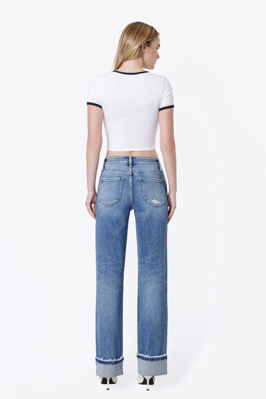 A woman shown from the back wearing a white cropped short-sleeve top with black trim and light blue wide-leg jeans, photographed against a plain white studio background.