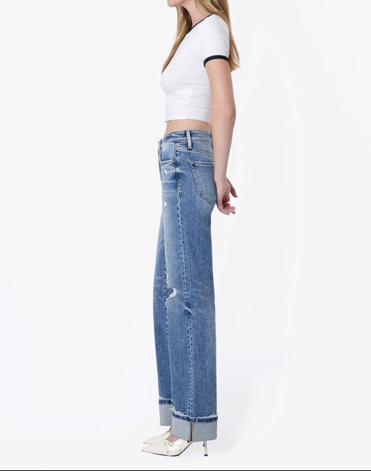 A woman shown in profile wearing light-wash blue wide-leg jeans, a white cropped short-sleeve top with black trim, and white pointed heels against a plain white studio background.