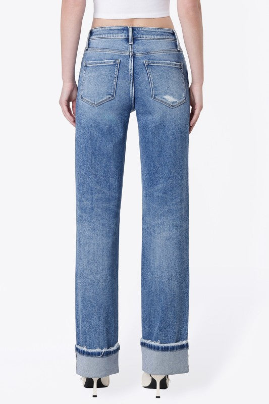 A person shown from the back wearing light blue wide-leg jeans with a raw, frayed hem and distressed details on the back pockets, paired with a white crop top and black heels, against a plain white background.