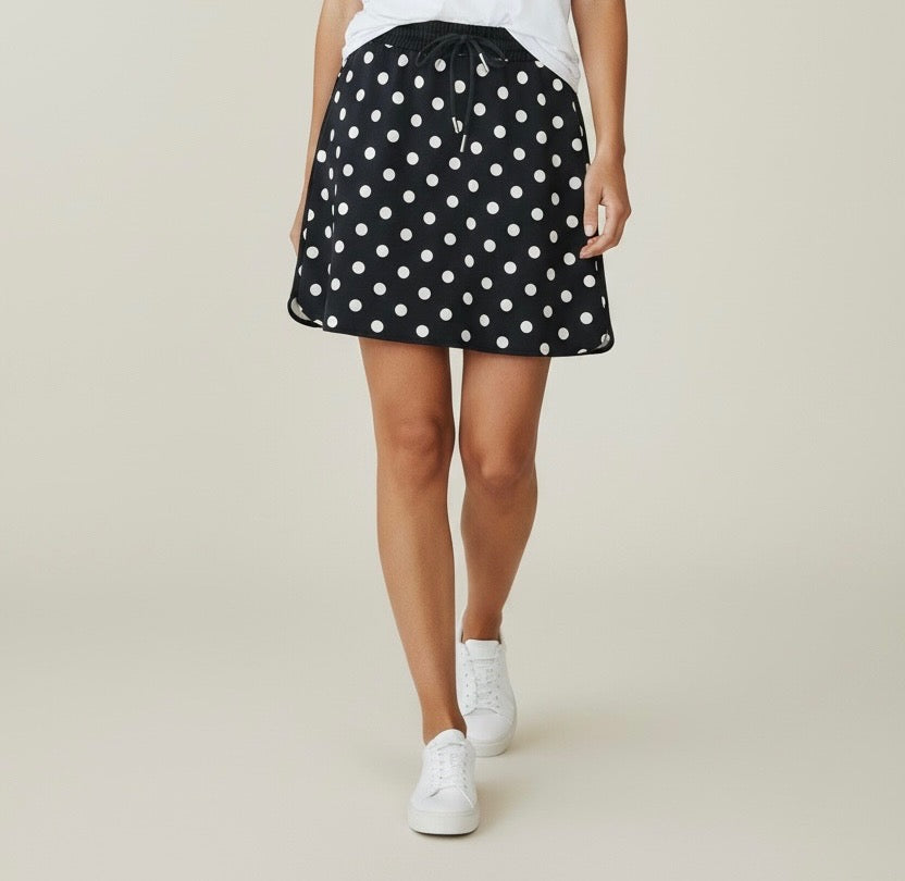 Person wearing a black polka dot skirt with white sneakers on a beige background