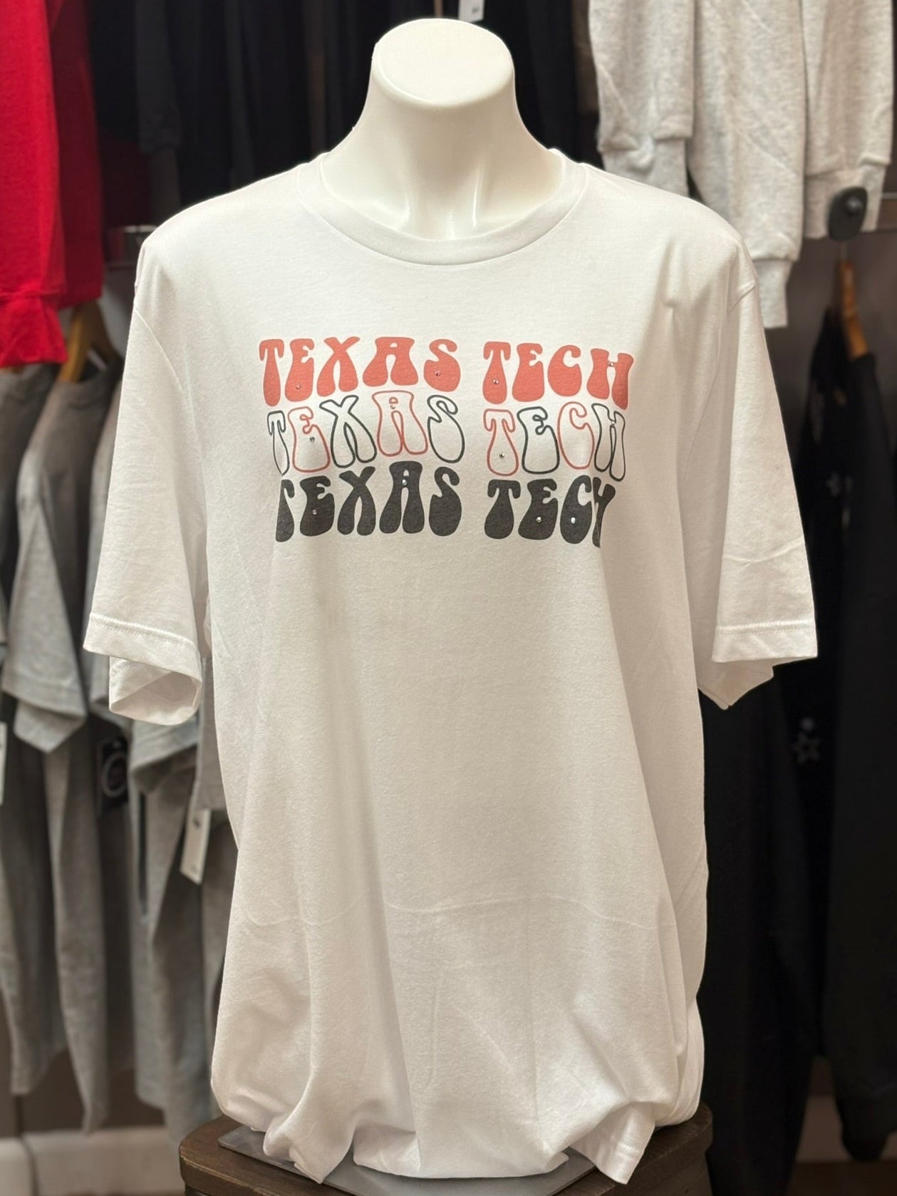 White t-shirt with 'TEXAS TECH' printed multiple times on a mannequin in a store setting.